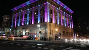 Un edificio histórico con ventanas arqueadas y techo plano, iluminado con luces moradas y azules.