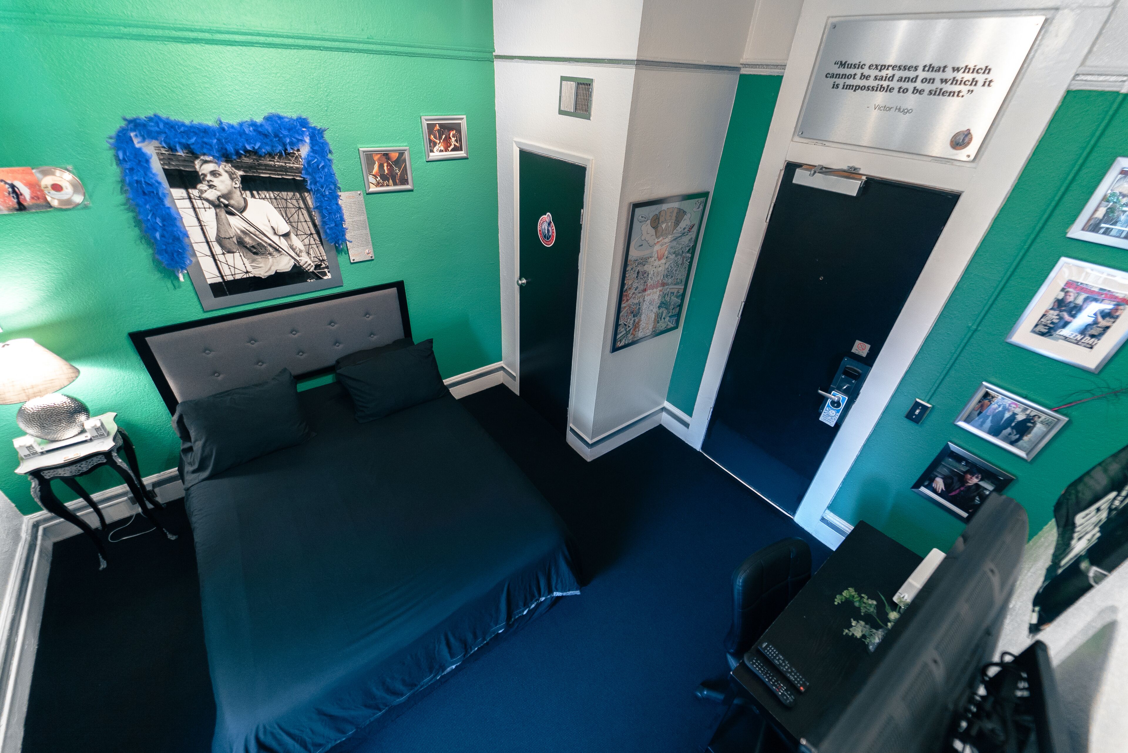 A room with a bed, a desk, and a door. There are posters on the walls and a quote on the door.