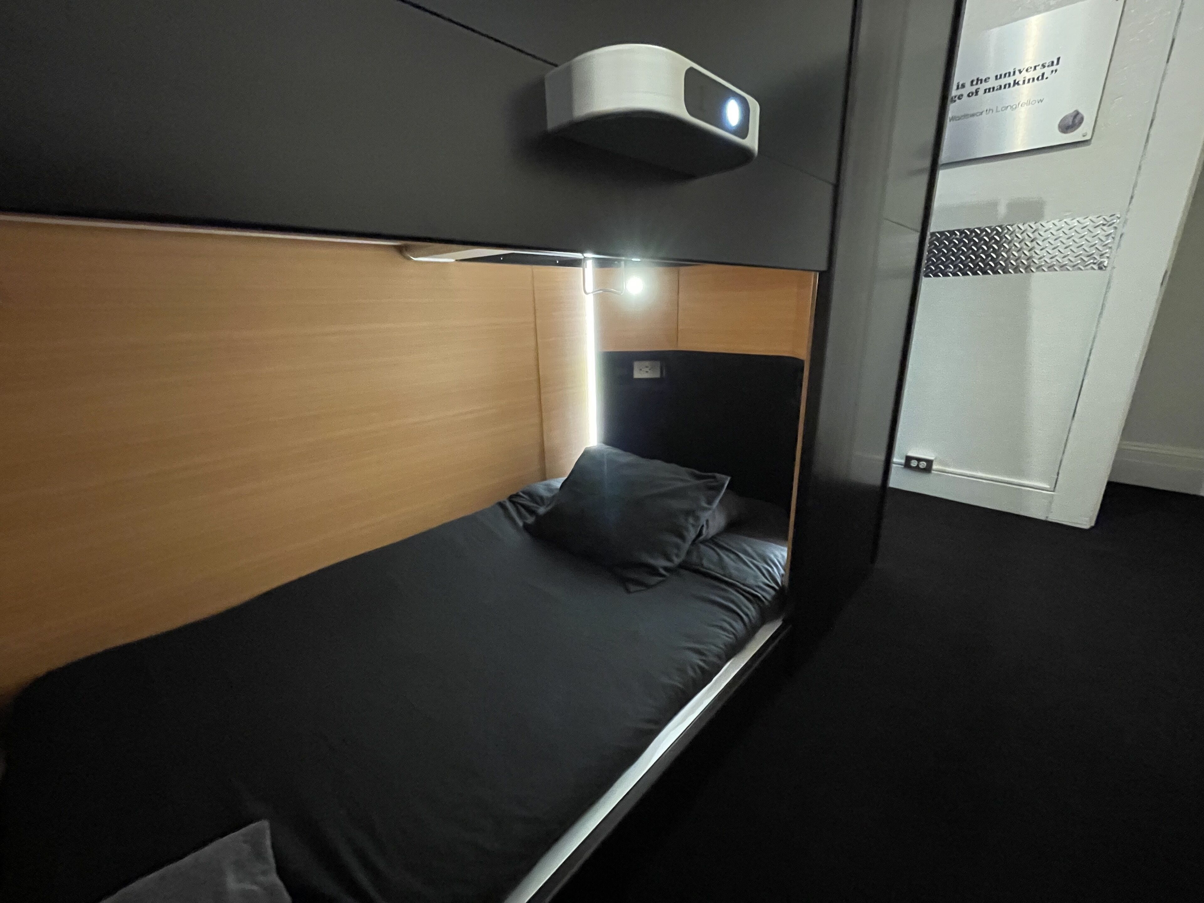 A modern hotel room with a single bed, a headboard with a built-in light, and a small bedside table.
