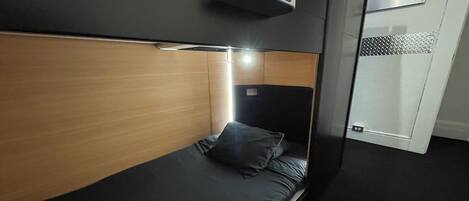 A modern hotel room with a single bed, a headboard with a built-in light, and a small bedside table.