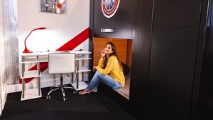 Una habitación con un escritorio, una silla, una estantería y un logotipo en la pared.