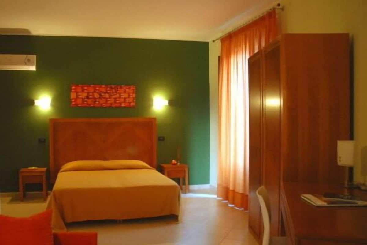 Ein Hotelzimmer mit einem großen Bett, zwei Nachttischen, einem Schreibtisch mit Stuhl und einer grünen Wand mit einer Dekoration.