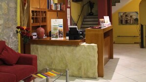 Un hall d’hôtel avec un comptoir d’accueil, un canapé rouge, une table en verre et un escalier.