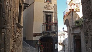 Une rue étroite, bordée de bâtiments des deux côtés, une enseigne indiquant l’« Hôtel del Pescador », et un petit balcon orné de plantes en pot.