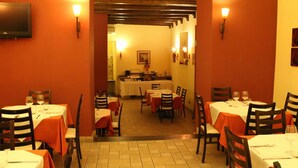 Un restaurant avec des tables dressées pour le service, une cuisine à l’arrière-plan et un téléviseur fixé au mur.