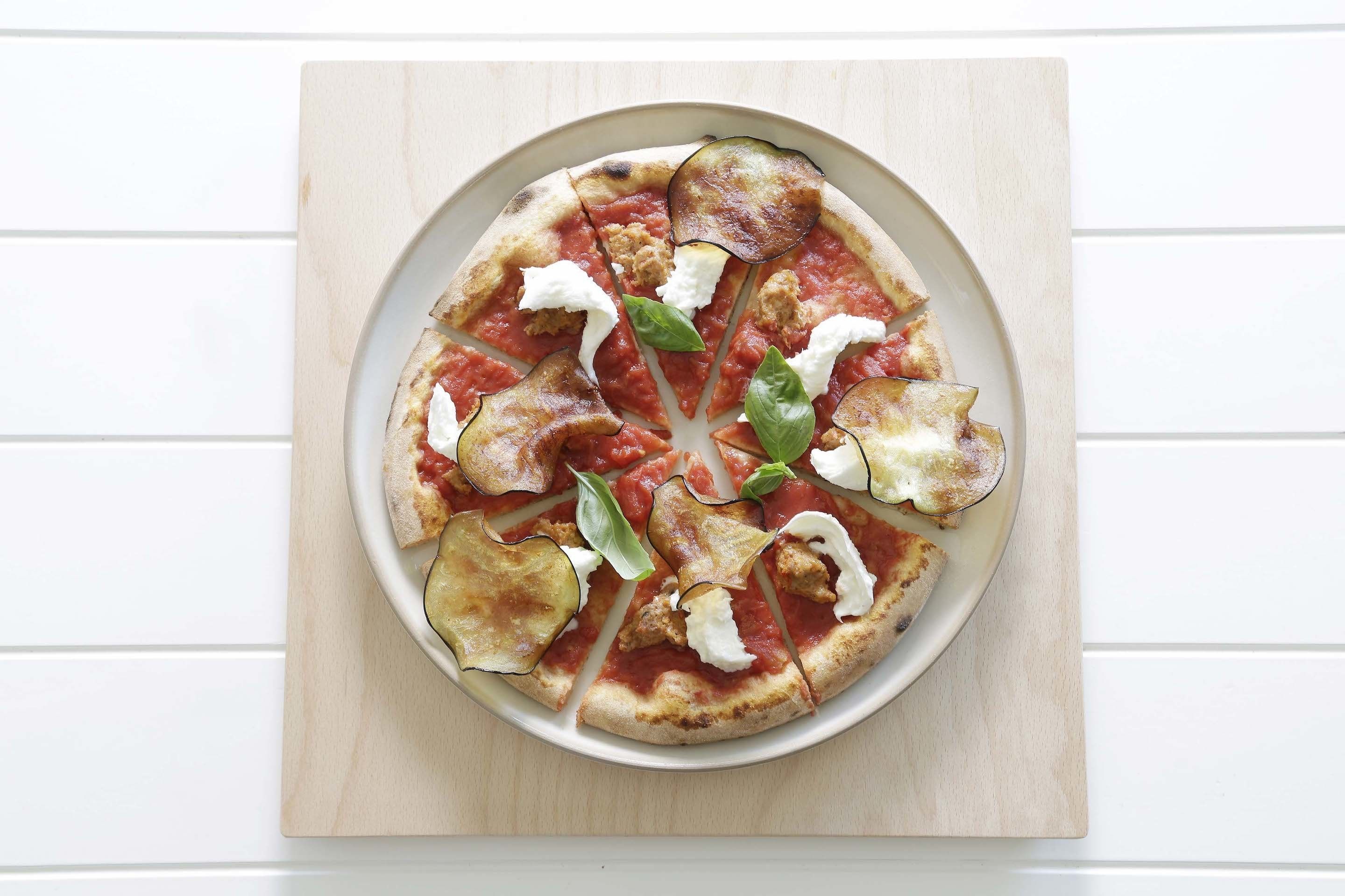 A pizza with tomato sauce, mozzarella, basil, and eggplant slices on a white plate.