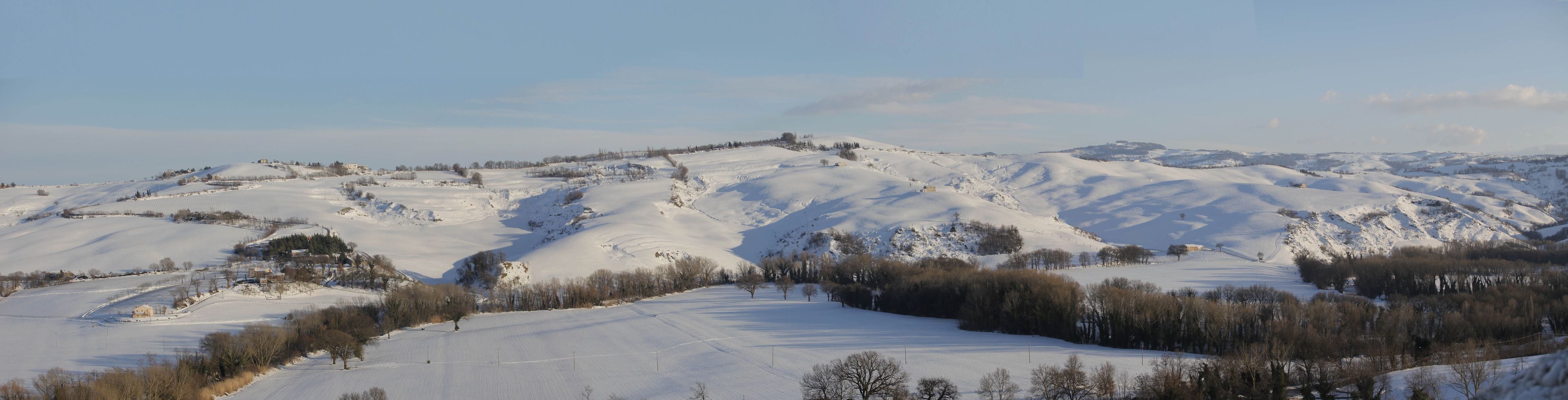 Ett snötäckt landskap med böljande kullar och fåtaliga träd.
