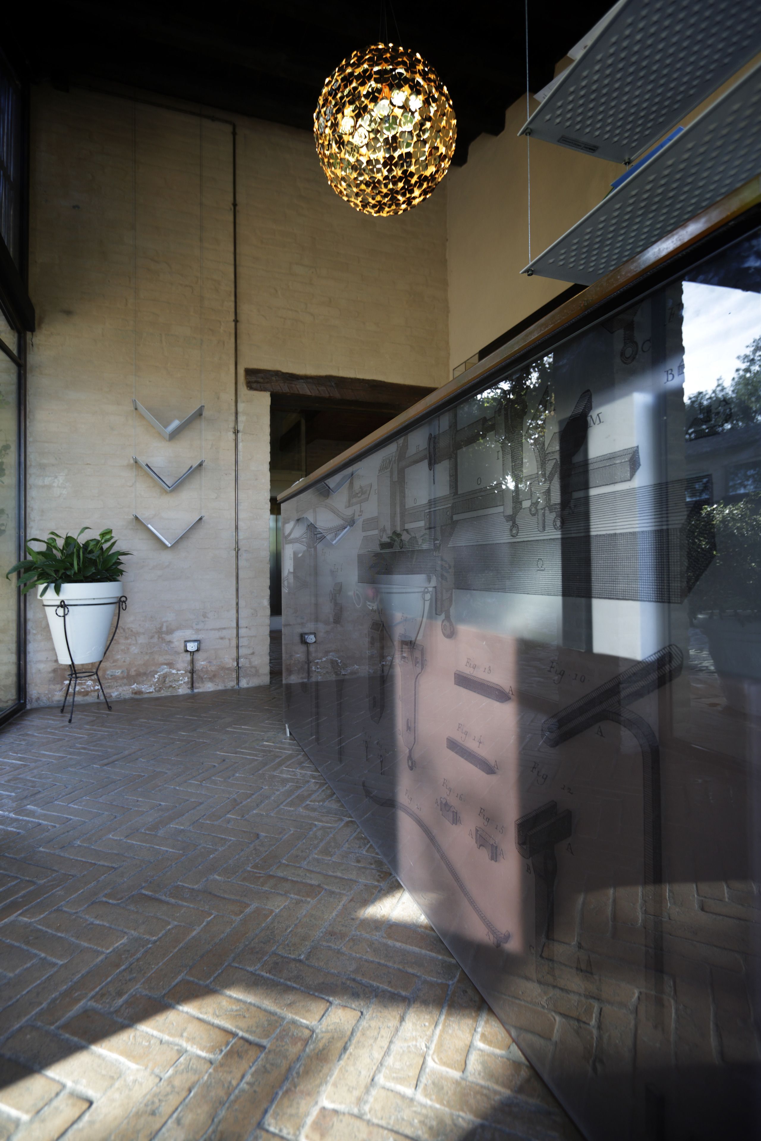 Un interior modern amb una làmpada esfèrica penjant, una planta en test i una paret de vidre que reflecteix l'exterior.