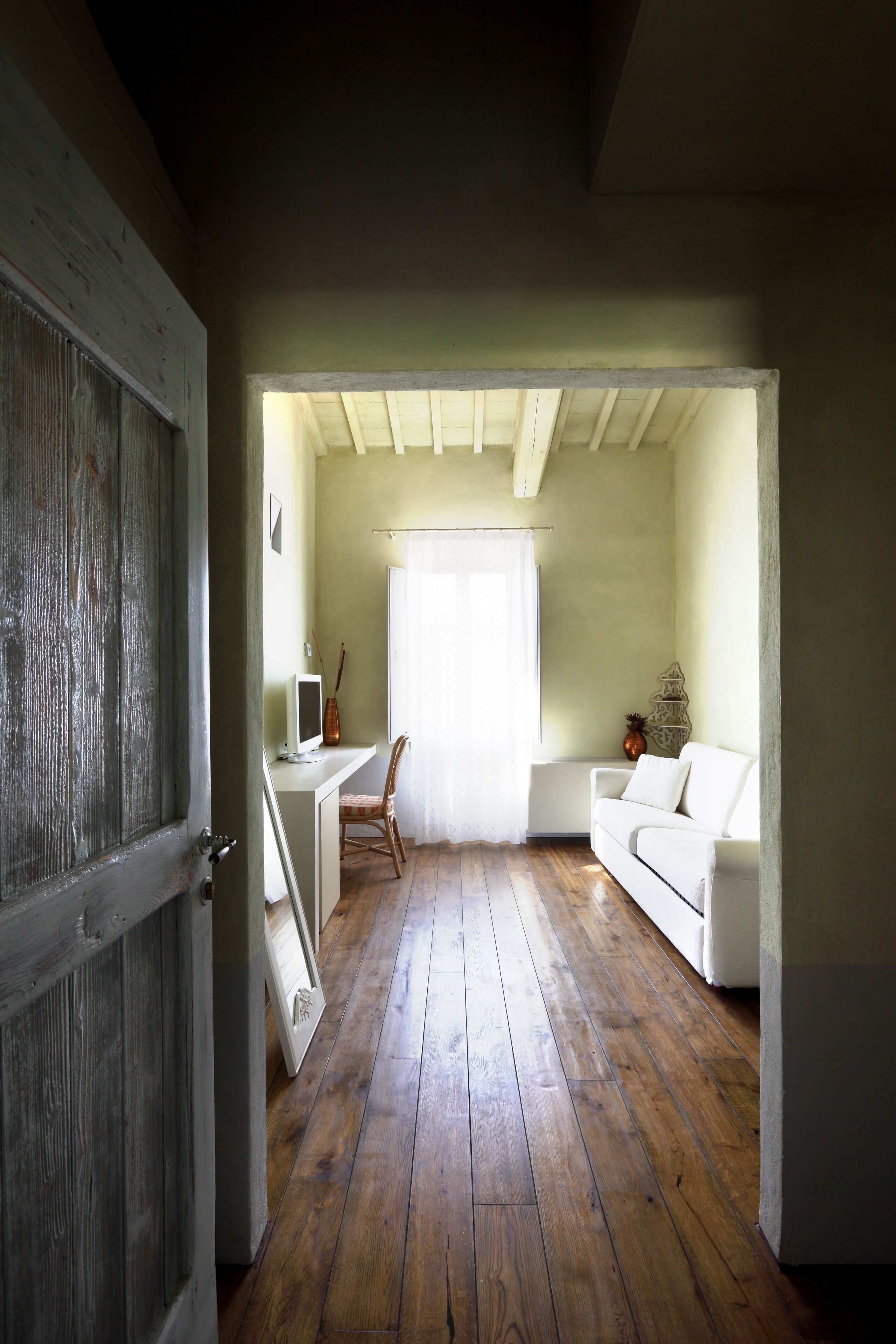 Una habitación con piso de madera, un escritorio blanco con una computadora, un sofá blanco y una silla.
