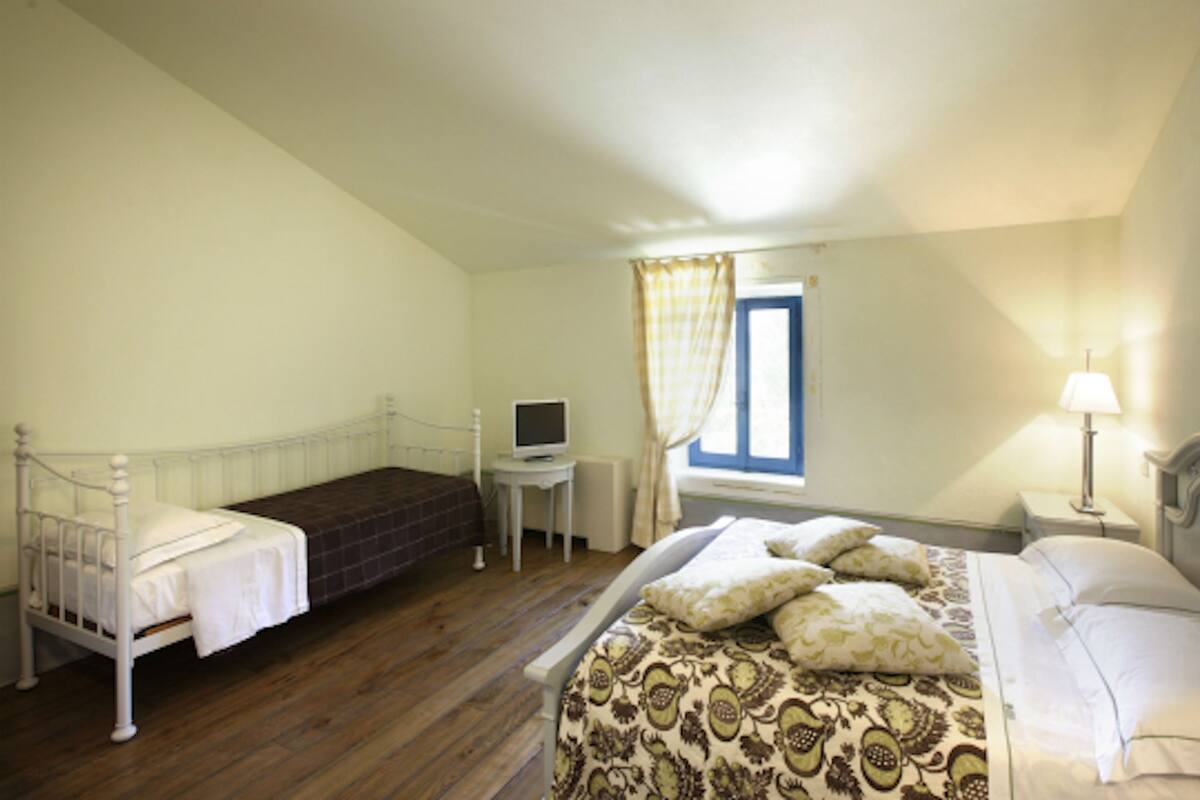 Une chambre à coucher avec un lit, un bureau avec un ordinateur, une fenêtre avec des rideaux et une lampe.