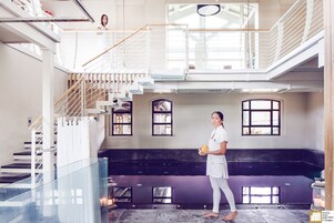 A spacious interior with a high ceiling, a staircase, and a person standing near a window.