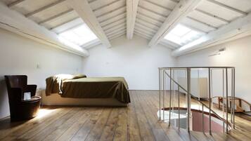 Une pièce aux hauts plafonds, dotée d’un plancher en bois, d’un lit, d’une chaise et d’une cloison en verre.