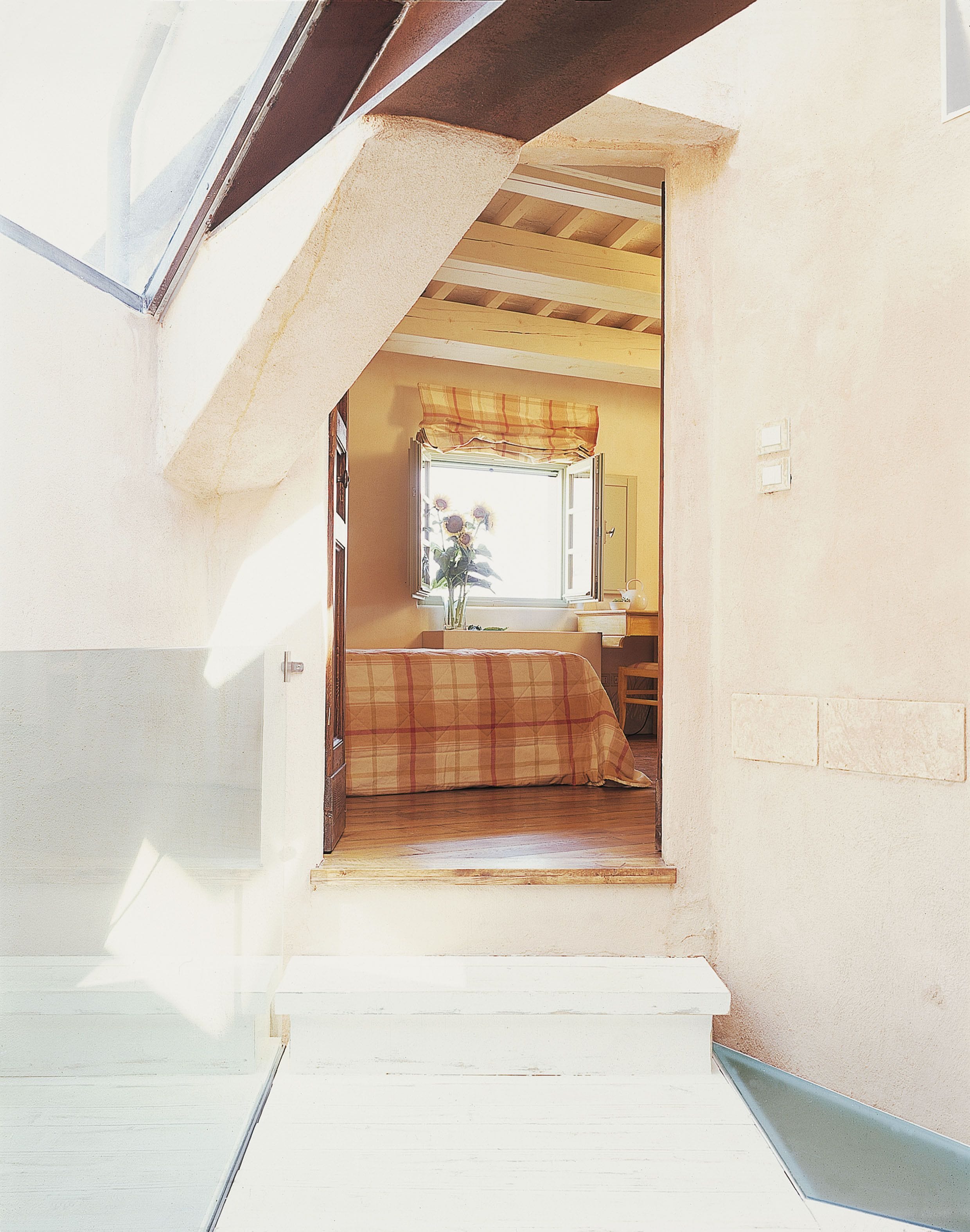 A narrow stairway leading to a bedroom with a window, a bed, and a nightstand.