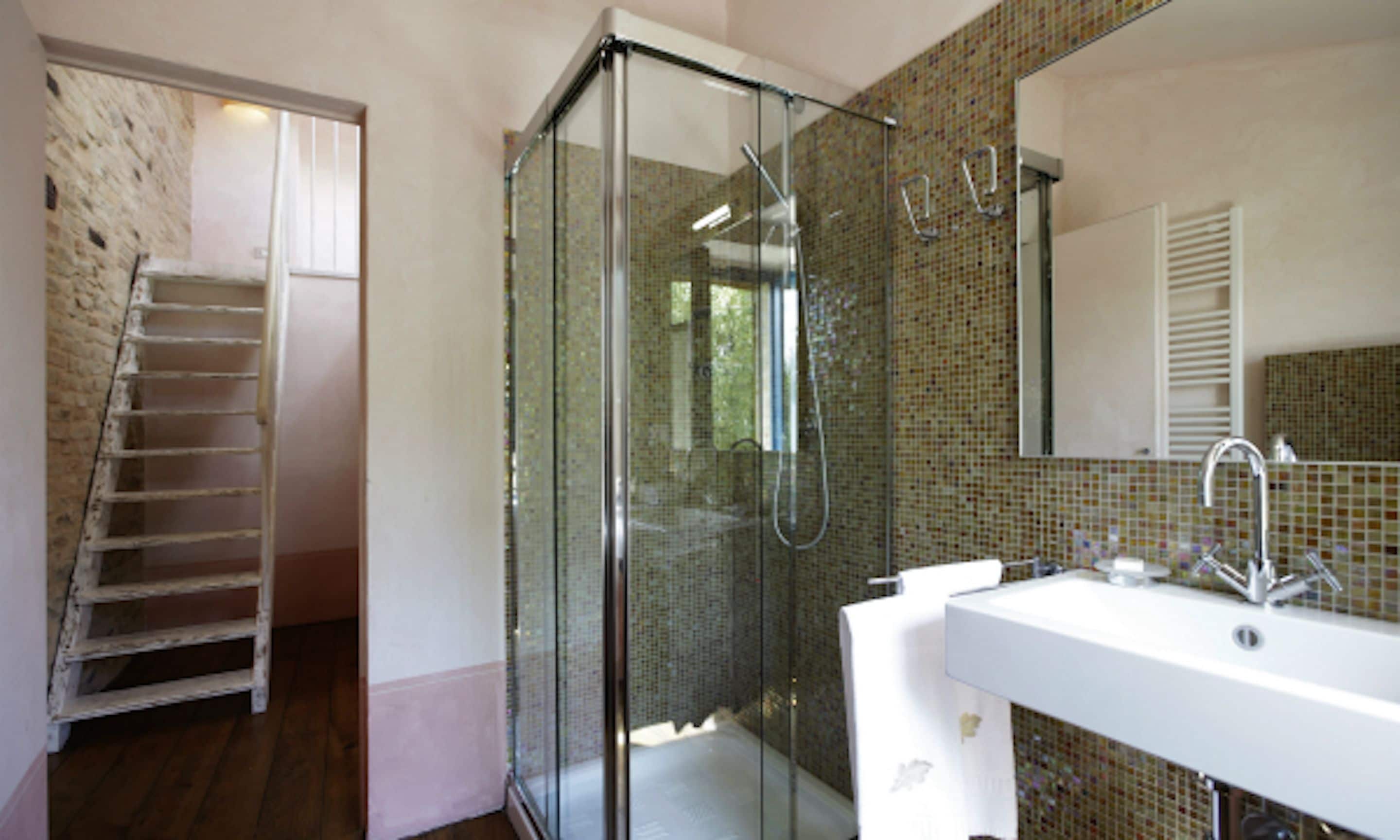 Ein modernes Badezimmer mit einer Glaskabine zur Dusche, einem weißen Waschbecken und einer gefliesten Rückwand.