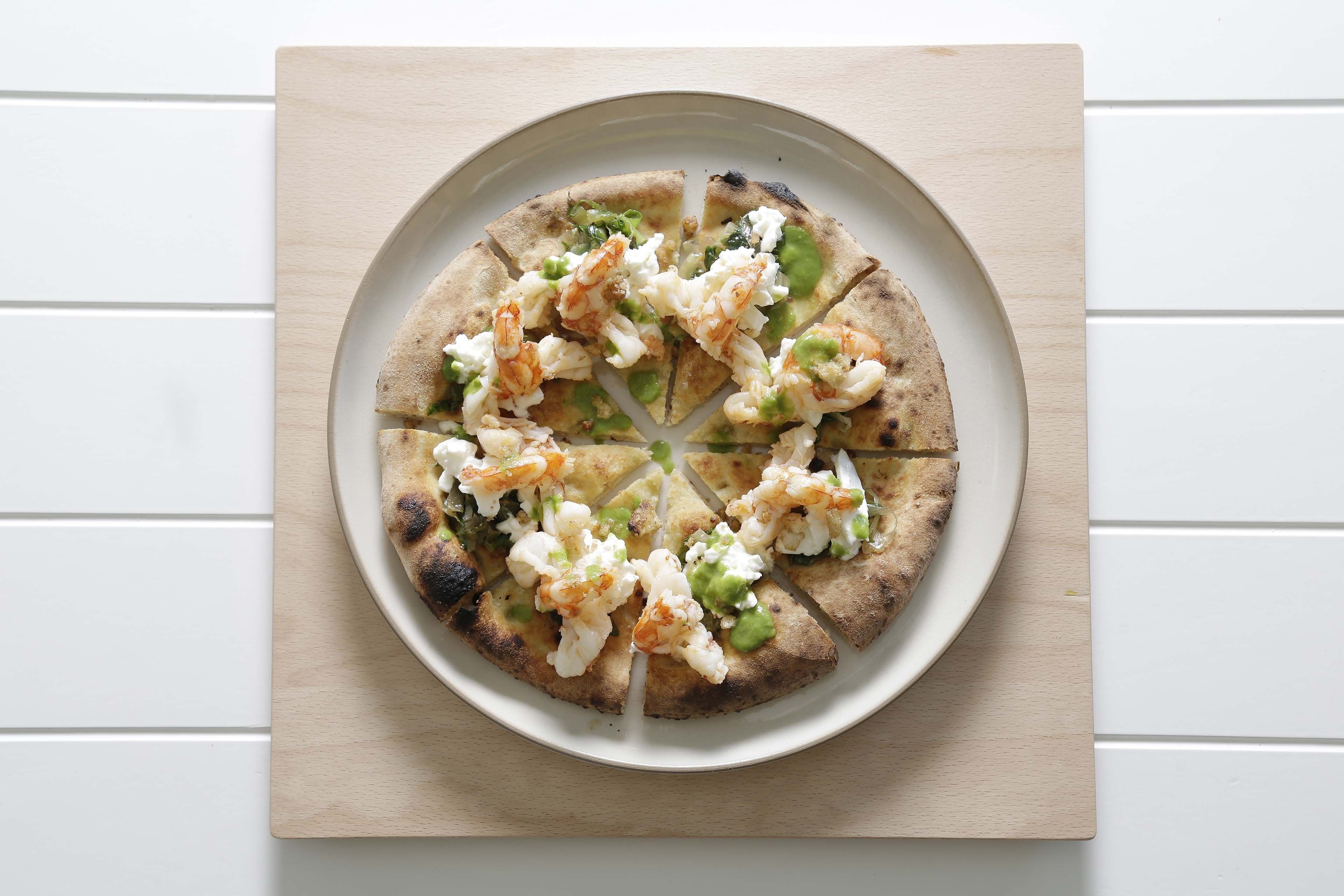 Une pizza sur une assiette blanche, posée sur une planche en bois.