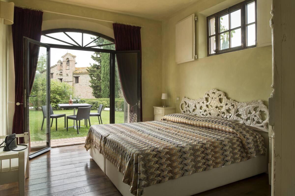 Une chambre avec un grand lit, une fenêtre et une vue sur un immeuble et un jardin.