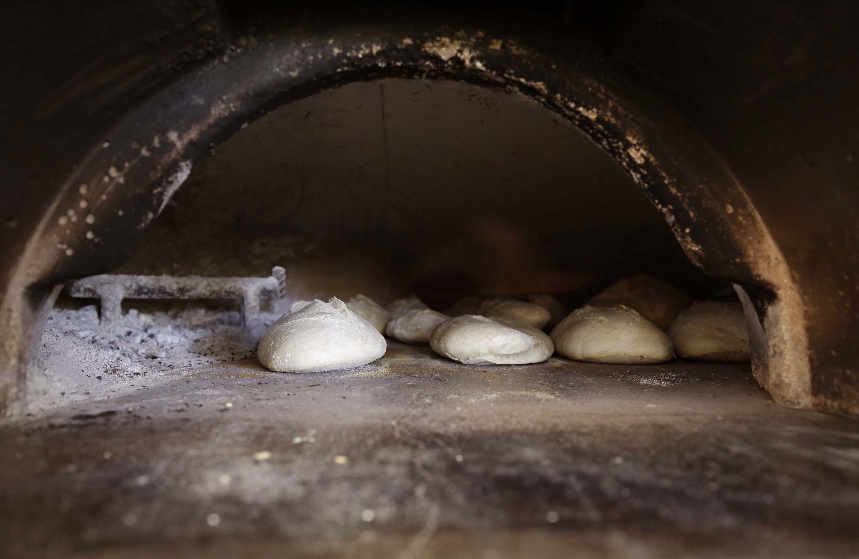 An arched brick oven with several loaves of bread baking inside.
