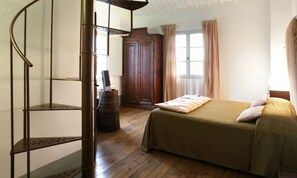 A bedroom with a wooden floor, a bed with a green bedspread, a wooden wardrobe, and a spiral staircase. - Tenuta Santi Giacomo e Filippo (Urbino)