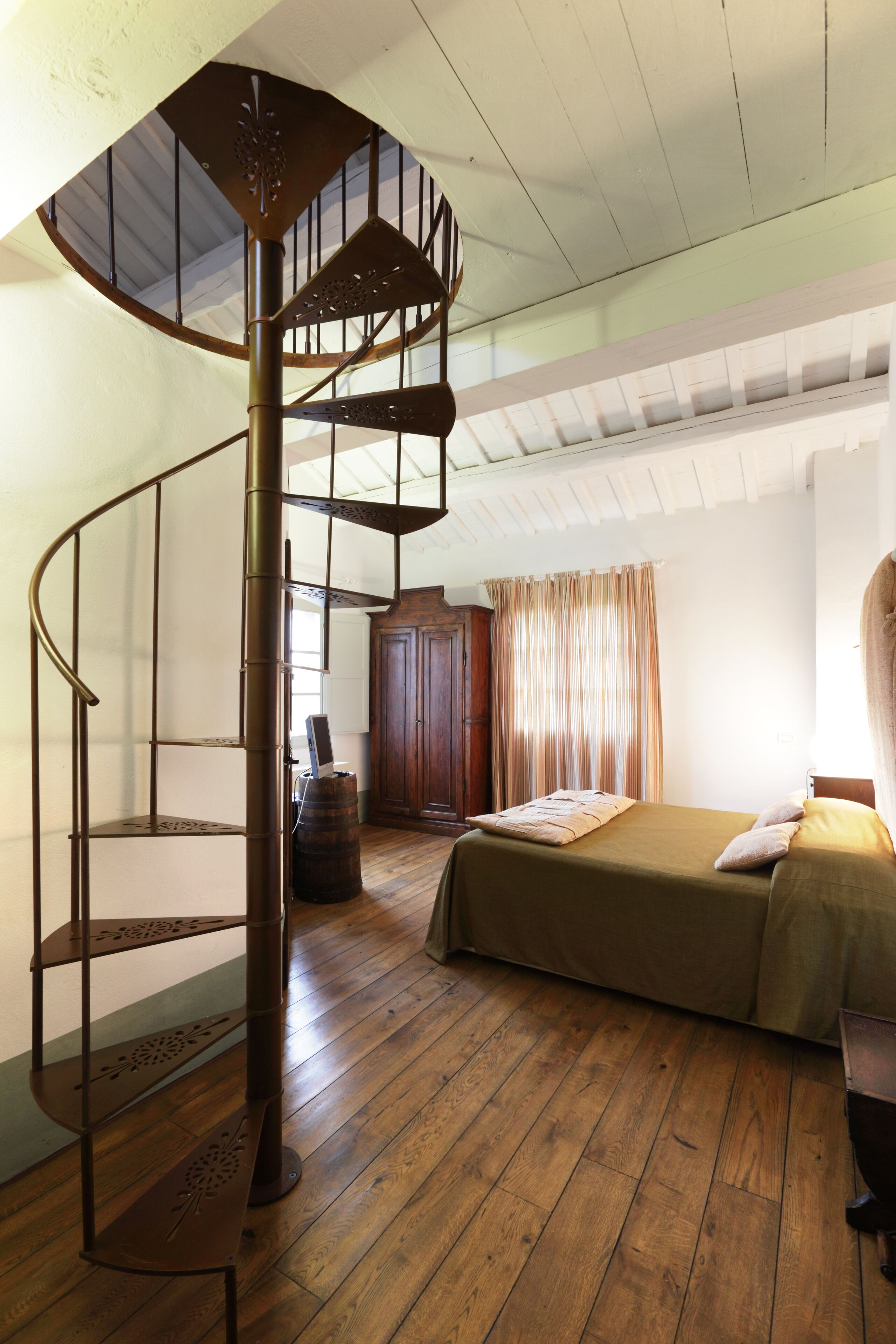 Eine Wendeltreppe in einem Raum mit Holzboden, einem Bett, einem Kleiderschrank und einem Fenster mit Vorhängen.