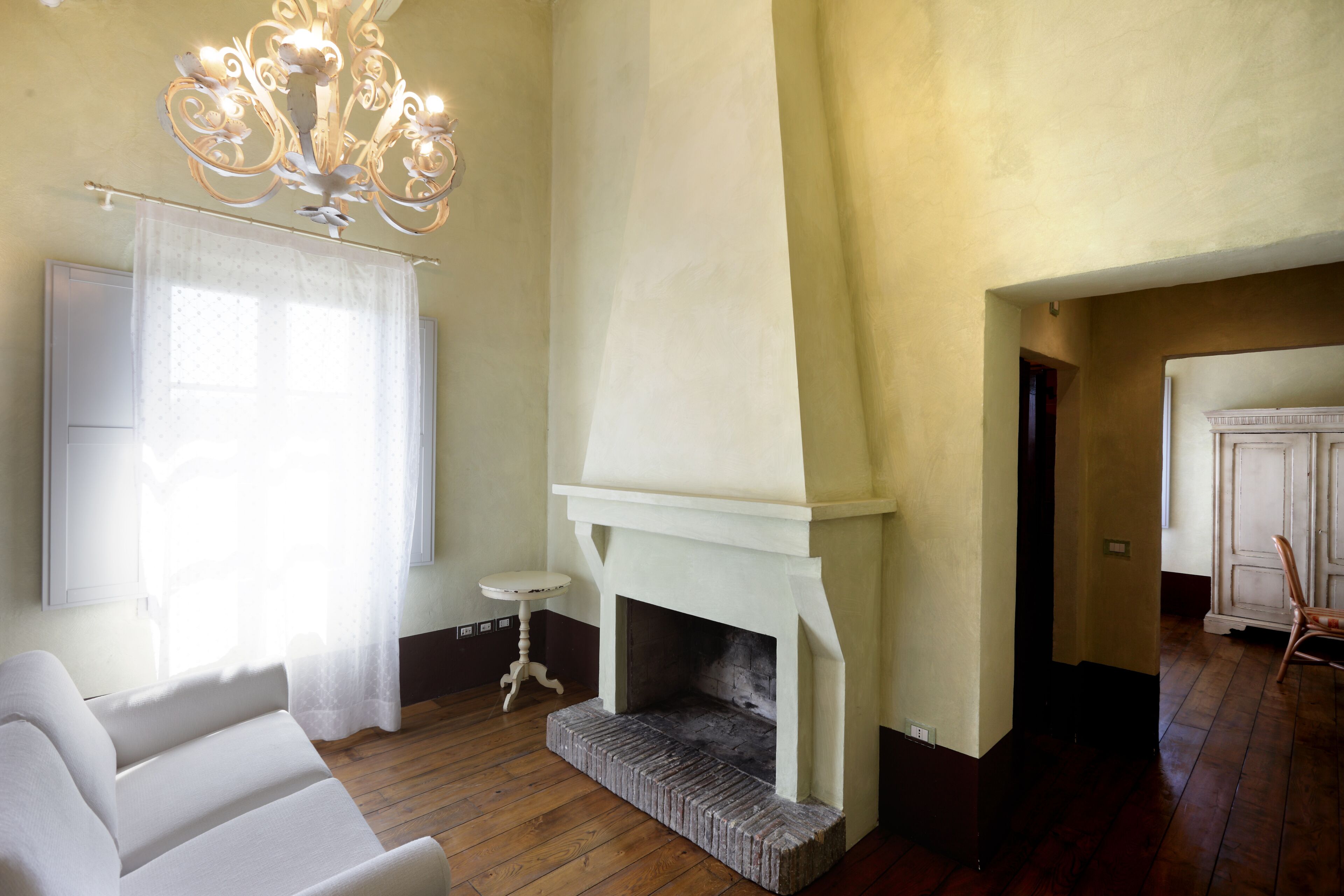 A room with a fireplace, a white sofa, a small table, and a chandelier.