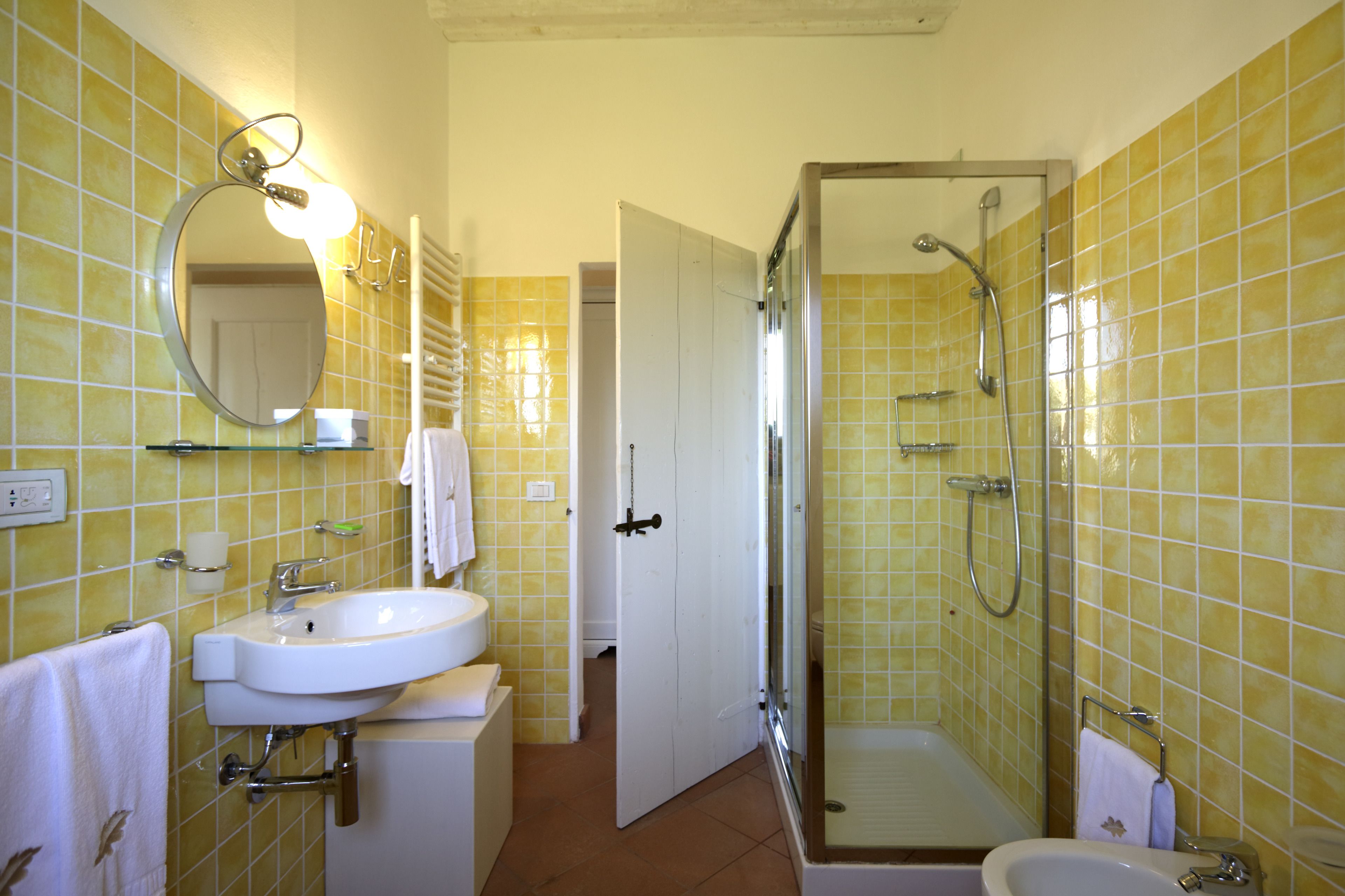 Une salle de bain avec des murs recouverts de carreaux jaunes, un lavabo blanc, un miroir et un espace douche.