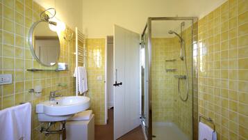 Une salle de bain avec des murs recouverts de carreaux jaunes, un lavabo blanc, un miroir et un espace douche.