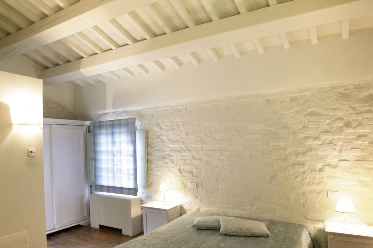 Une chambre à coucher avec un lit, une fenêtre avec un rideau, une table de chevet et un radiateur.