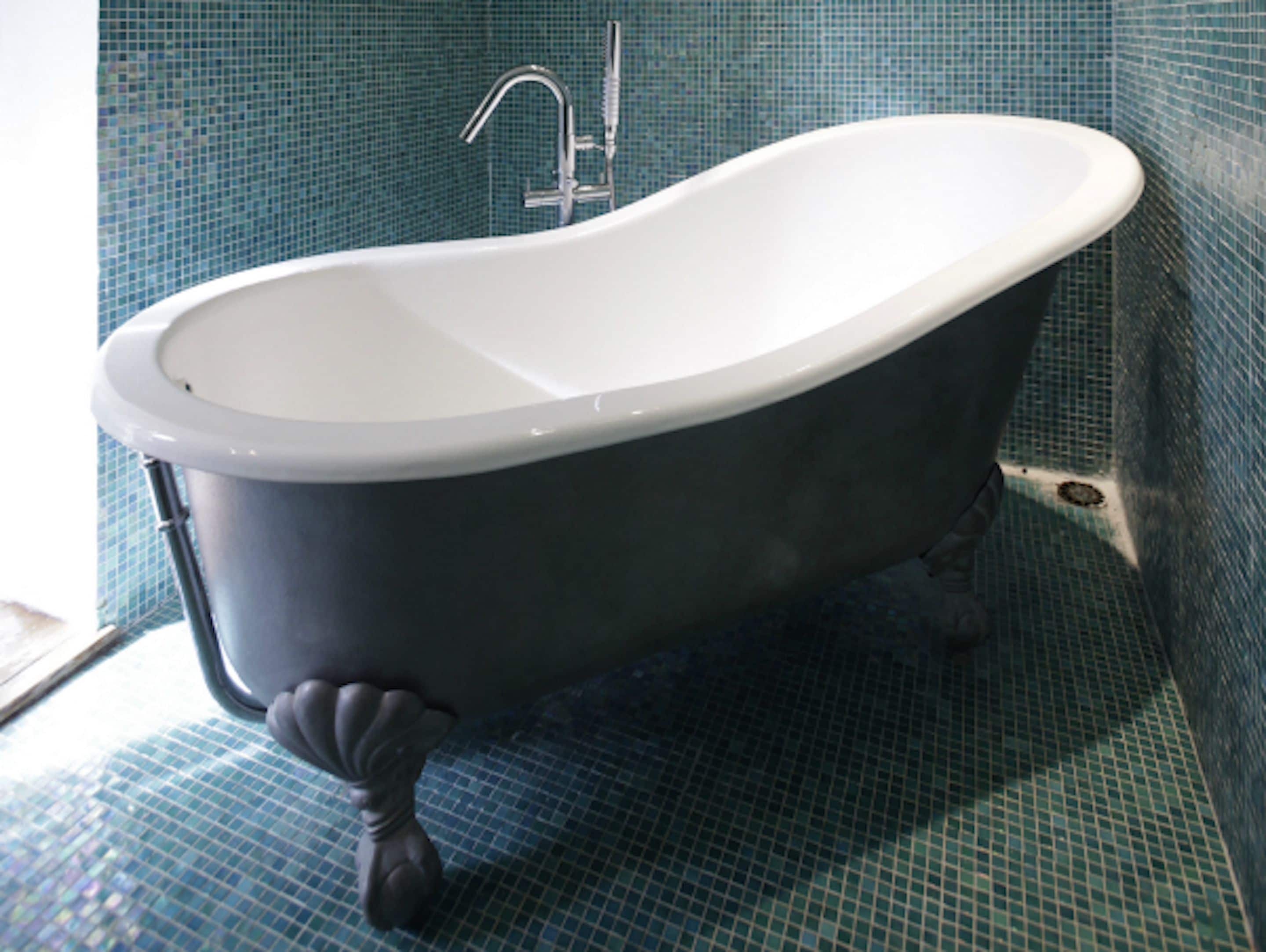 Una bañera independiente con patas de garra en un baño con paredes de mosaico azul.