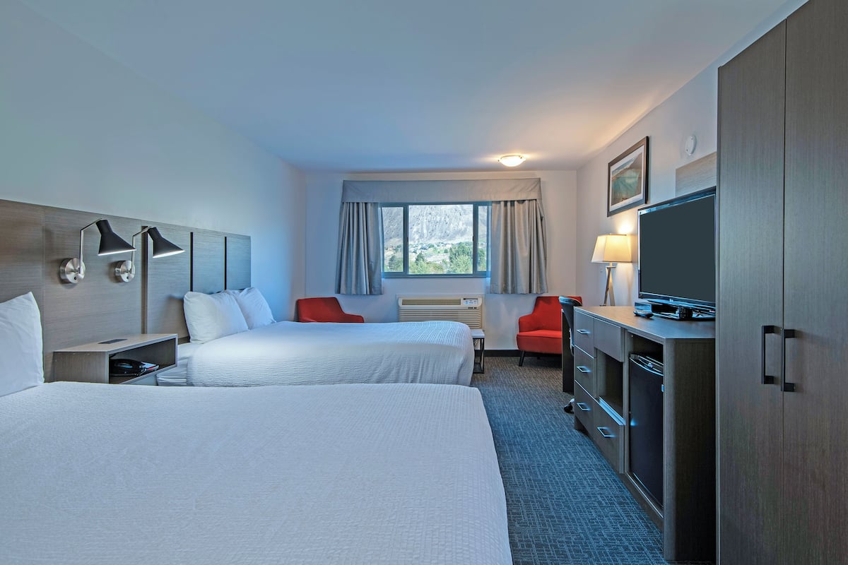 Une chambre d’hôtel avec deux lits, une télévision, un bureau, une chaise et une fenêtre avec des rideaux.