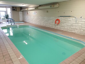 An indoor swimming pool with a tiled floor, a lifebuoy, and a wall with a stone pattern. - Riverland Inn & Suites (Kamloops)