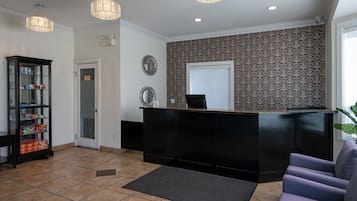 A reception area with a black reception desk, a glass display cabinet, a grey sofa, and patterned wallpaper.