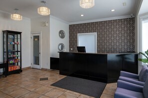 A reception area with a black reception desk, a glass display cabinet, a grey sofa, and patterned wallpaper. - Riverland Inn & Suites (Kamloops)