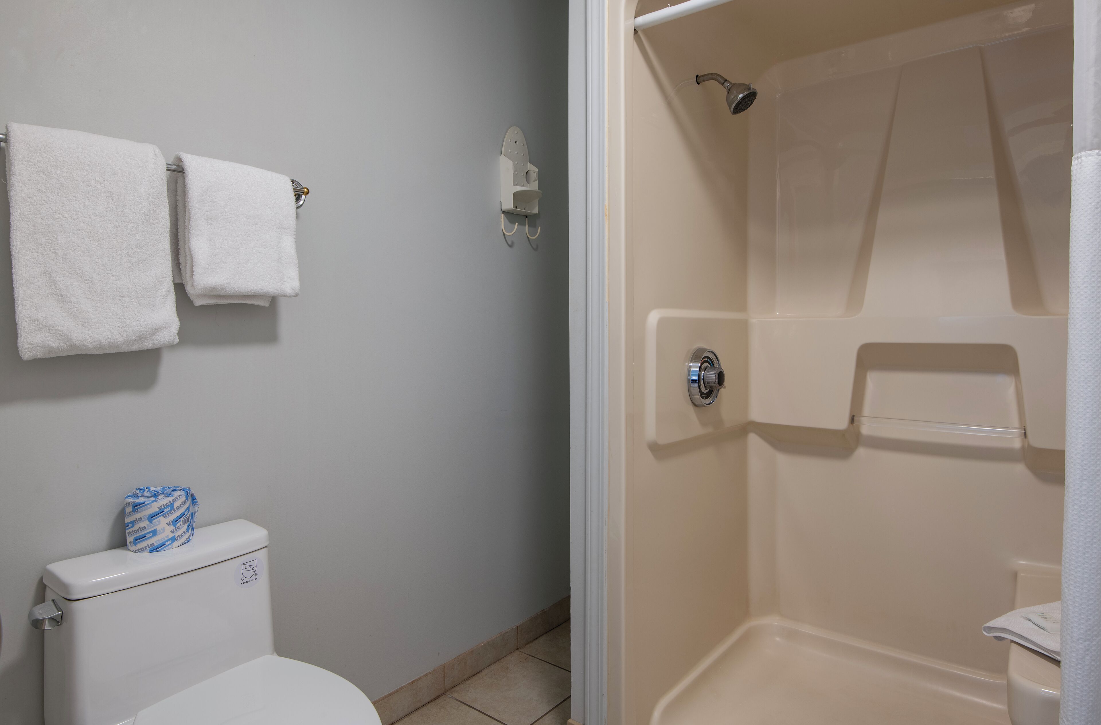 Un baño con inodoro, ducha y dos toallas colgadas en un perchero.