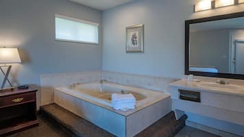 Ein modernes Badezimmer mit einer großen Badewanne, einem Waschtisch mit Spiegel und einem Fenster mit Jalousien.