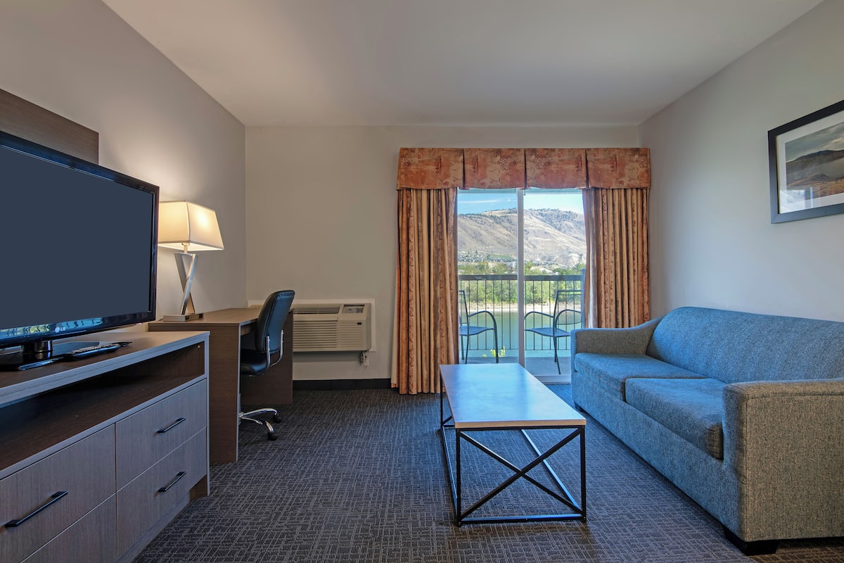 Une chambre d’hôtel équipée d’une télévision, d’un bureau, d’une chaise, d’un canapé et offrant une vue sur les montagnes par la fenêtre.