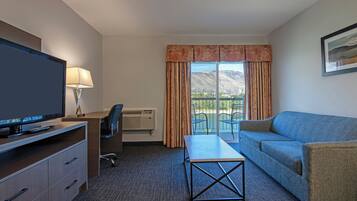A hotel room with a television, desk, chair, sofa, and a view of mountains through the window.