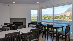 Un comedor con mesas y sillas, chimenea y amplios ventanales con vistas a un lago y montañas.