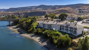 Un hotel con un edificio grande, cerca de un río y rodeado de árboles y colinas.