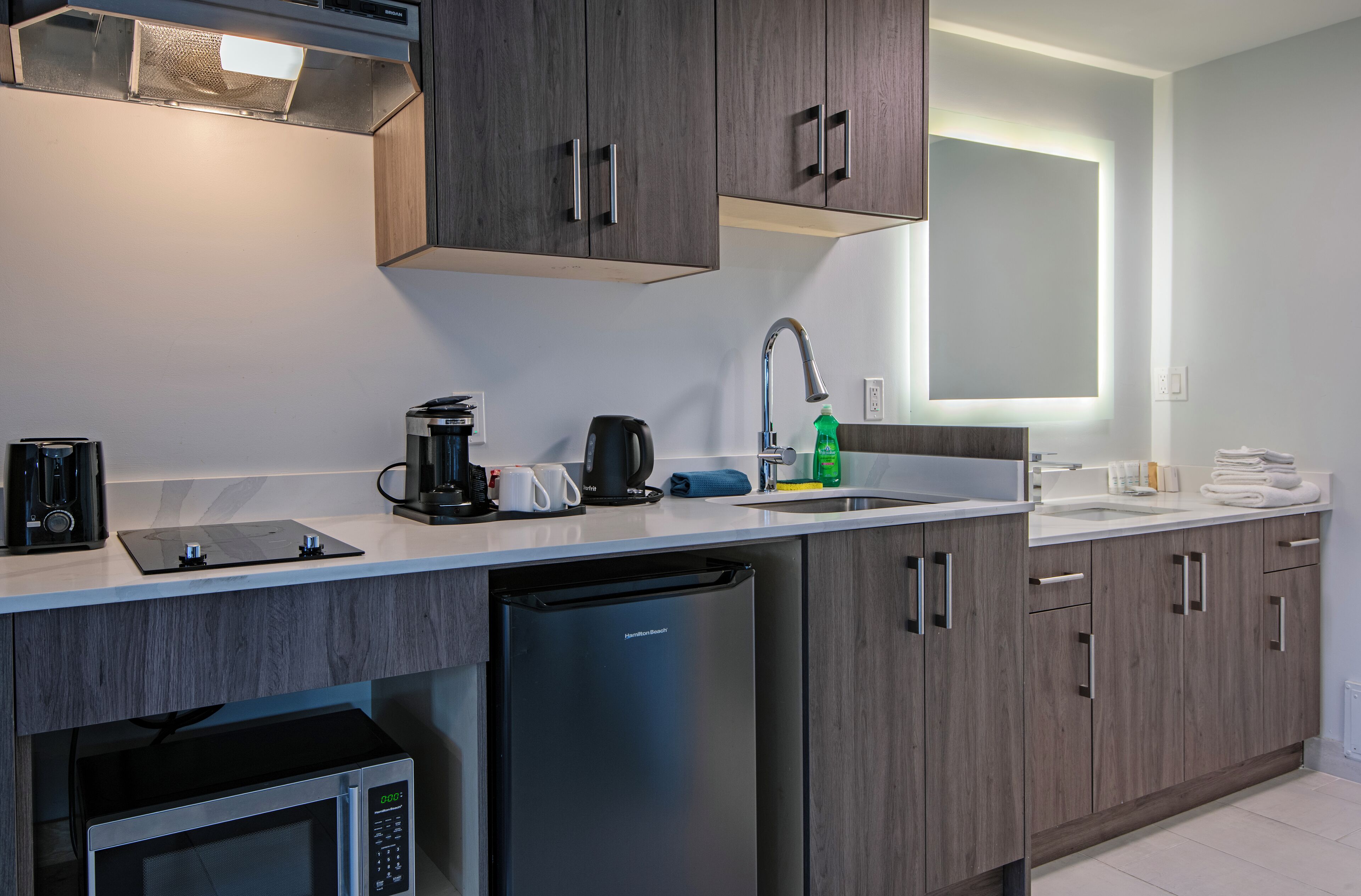 Una cocina moderna con armarios de madera oscura, lavavajillas integrado, microondas, cafetera y un lavabo con grifo.