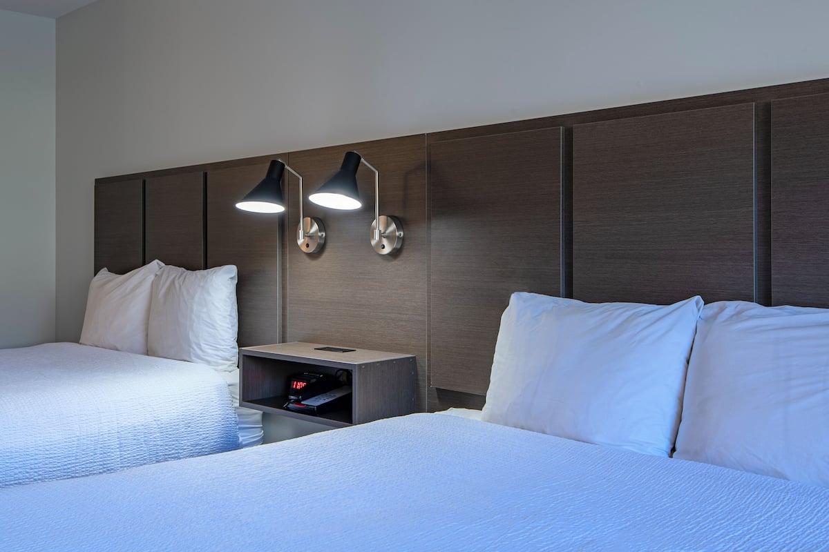 Une chambre d’hôtel avec deux lits, une table de chevet avec une lampe et un téléviseur intégré.