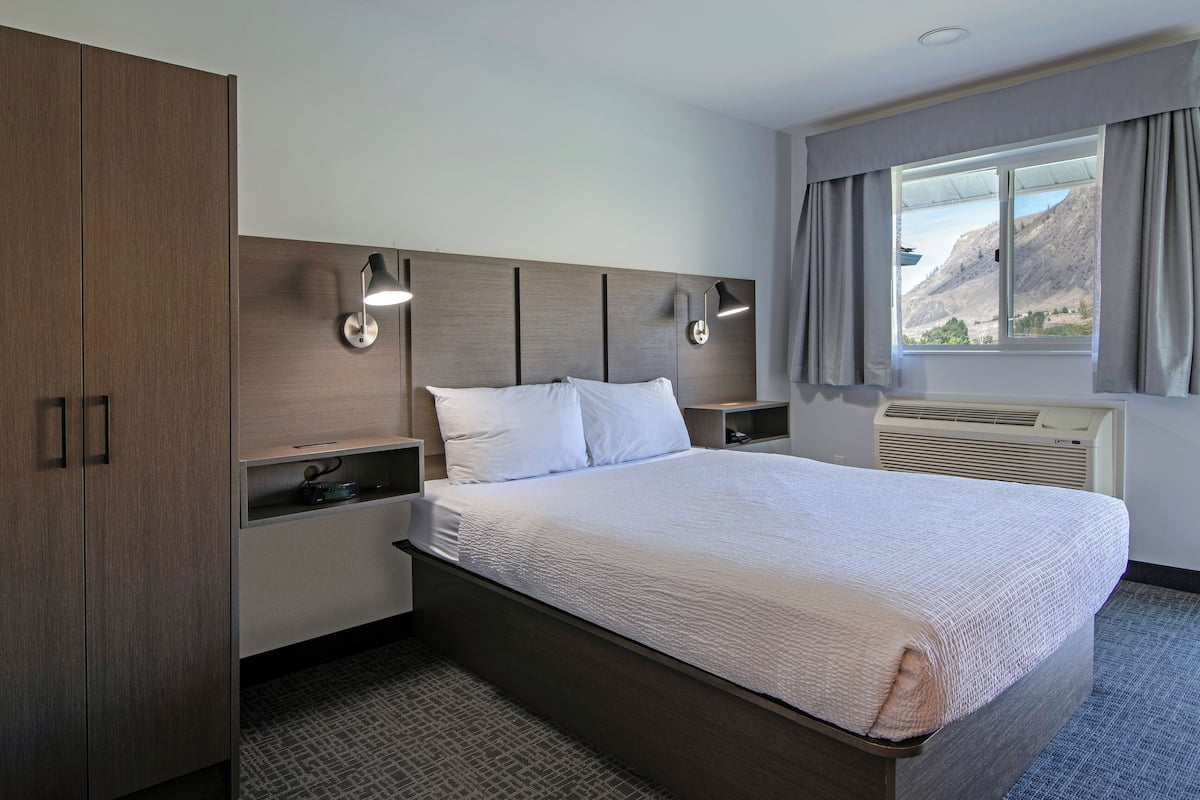 Une chambre d’hôtel avec un grand lit, une armoire en bois, des lampes de chevet, une fenêtre avec des rideaux et un appareil de climatisation.
