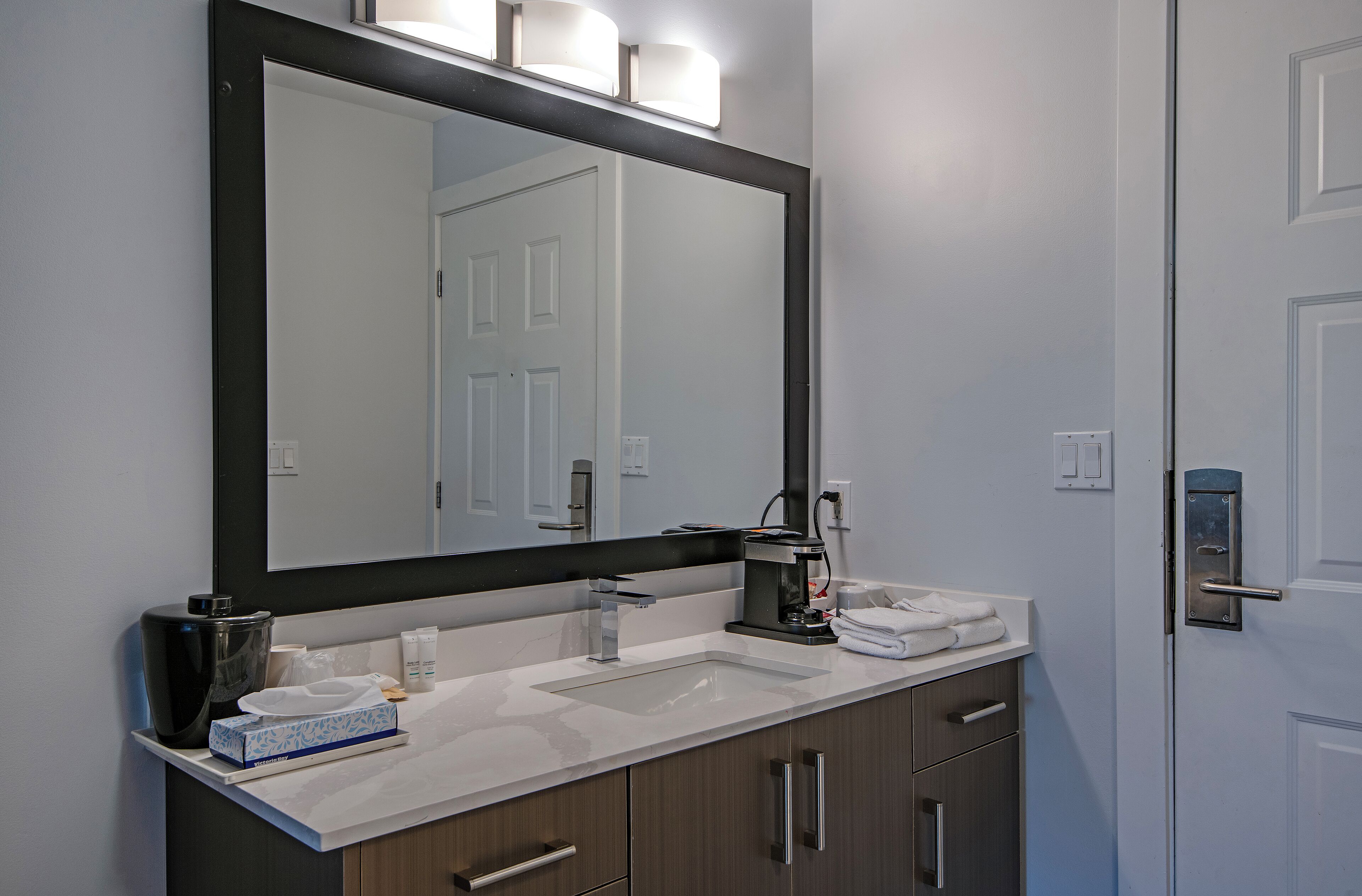 A bathroom with a large mirror, a sink, a coffee maker, and a towel rack.