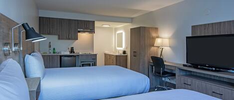 A hotel room with two beds, a desk, a TV, and a kitchenette.