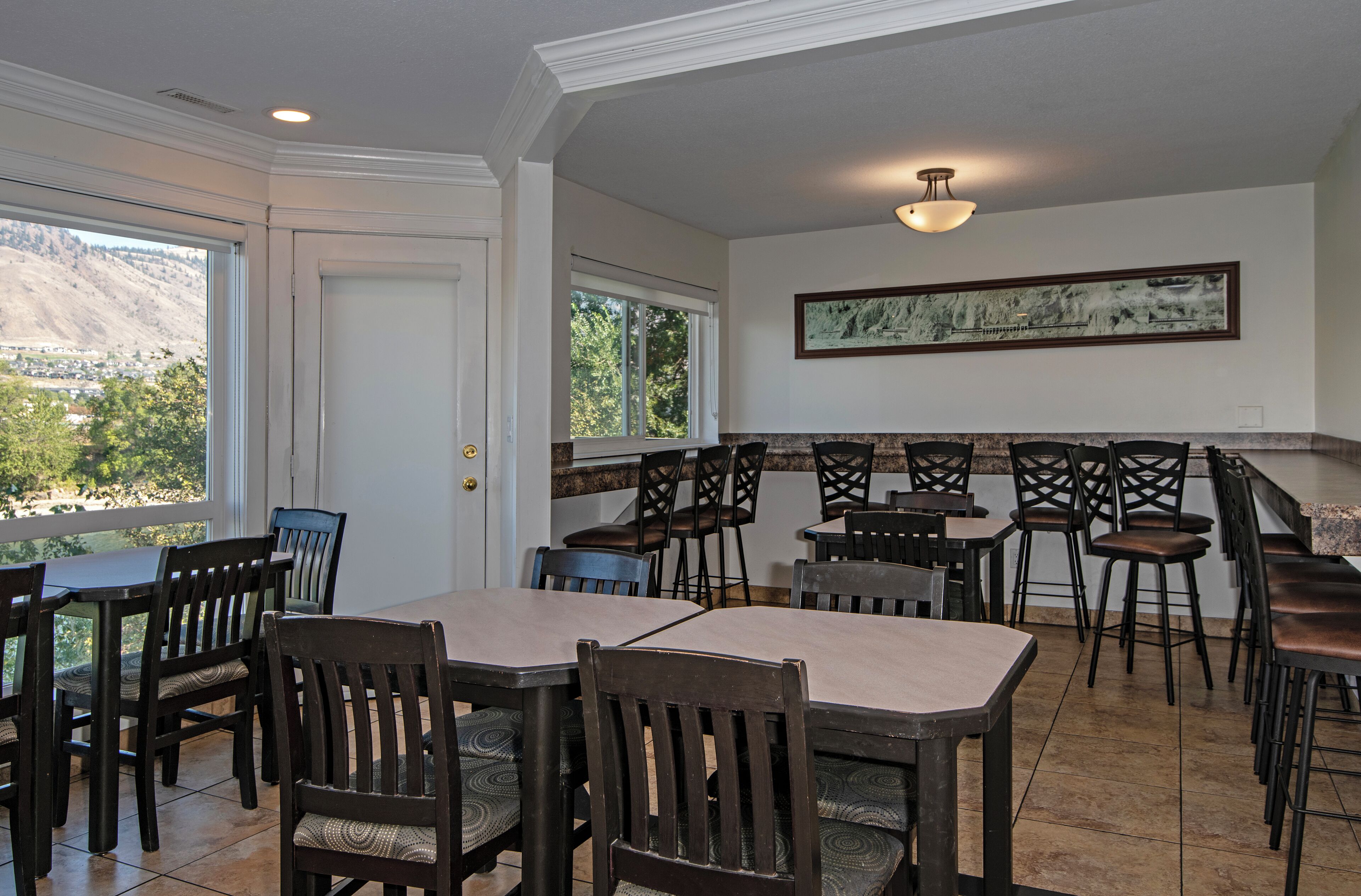 A dining area with multiple tables and chairs, a view of a mountain, and a framed artwork on the wall.