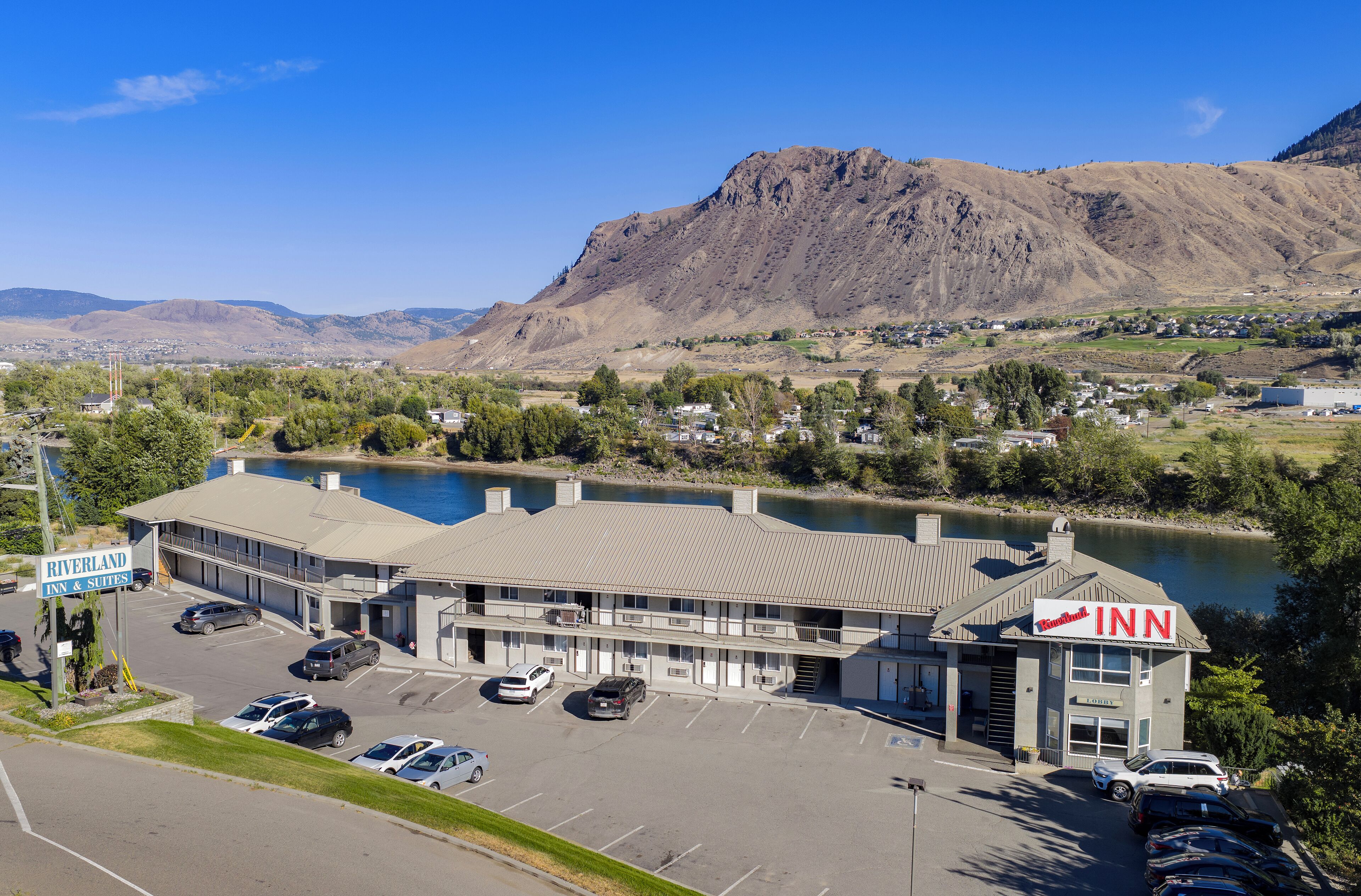 A Riverland Inn & Suites with a parking lot, a view of a lake, and mountains in the background.
