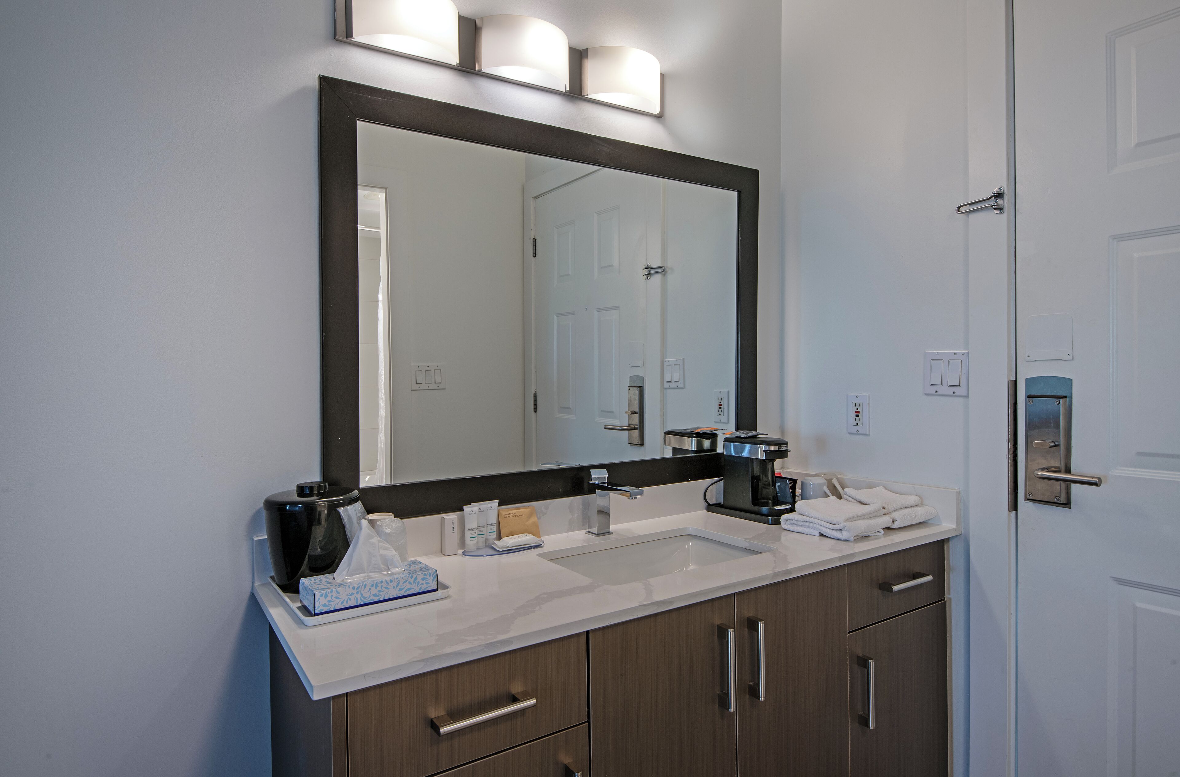 Une salle de bain moderne avec un grand miroir, deux lavabos et une machine à café.