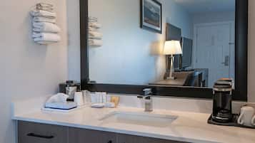 A hotel bathroom with a sink, mirror, towels, toiletries, and a coffee maker.