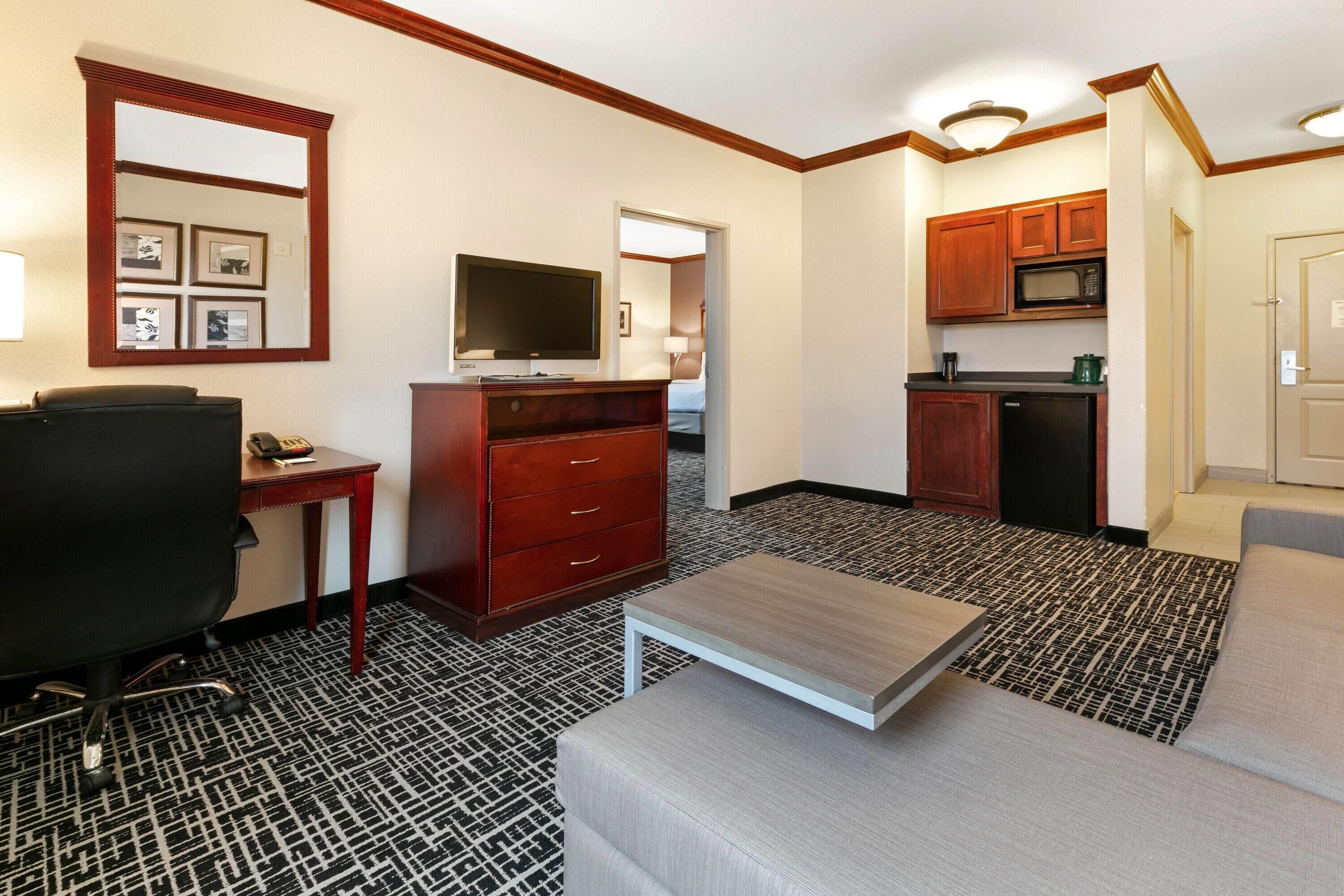 Een hotelkamer met een kitchenette, een televisie, een bureau, een stoel en een bank.