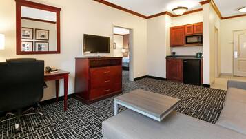 Habitación de hotel con kitchenette, televisor, escritorio, silla y sofá.