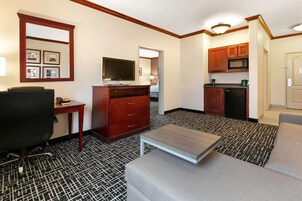 Habitación de hotel con kitchenette, televisor, escritorio, silla y sofá.